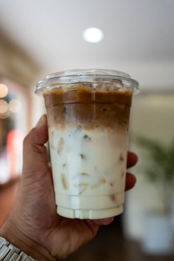 İki kat taze süt ve espresso ile buzlu latte kahve tutan bir el. Yaz içeceği konseptini tazelemek