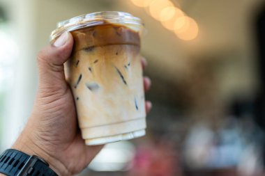 Adamın elinde plastik bardak buzlu kahve var. Üst katmanda esspeso var. Altında taze süt, seçici odak noktası..