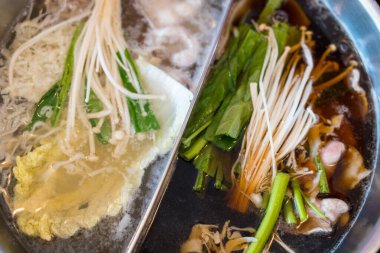 İkiye bölünmüş, domuz eti, sebze ve mantarlar da dahil olmak üzere lezzetli et suyu ve çeşitli malzemelerle dolu bir tencerenin yakın çekim görüntüsü.