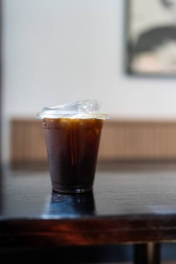 Plastik bir bardak buzlu Americano ya da ahşap masada sade kahve.