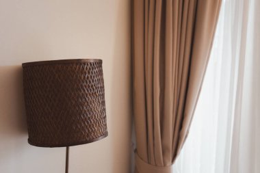 Evdeki kahverengi perdenin yanında güzel, modern, ayakta duran rattan ışığı.