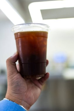 Ofisteki adam şeffaf plastik bardakta buzlu americano tutuyor.