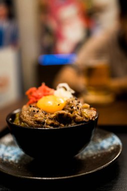 Wagyu bifteği pilavı ve çiğ yumurta kasesi, kremalı yumurta sarısı leziz bifteği kucaklıyor, dokuların ve tatların lezzetli bir harmonisine karışıyor siyah bir kasede..