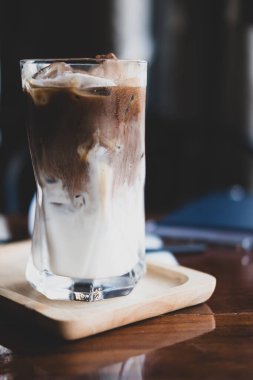 Kafenin ahşap masasında taze sütle uzun bir bardakta buzlu Mocha kahvesi.