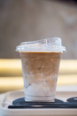Bir bardak buzlu latte, beyaz tahta tepside, şeffaf plastik bir bardakta süt.