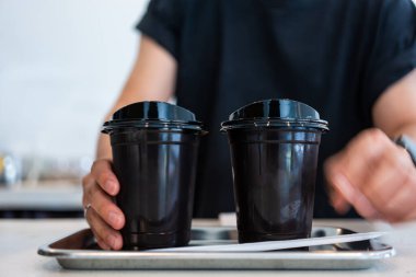 Barista kahve dükkanındaki müşterilere iki plastik kahve servisi yaptı.