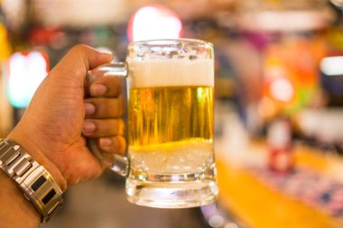 Elinde bir bardak bira tutan bir adam. Gençlerin havalı bir barda birlikte eğlenmesi konsepti. Orta bardağa odaklan.