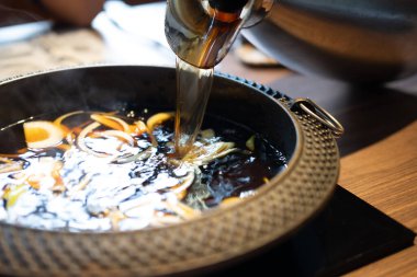 Sıcak tencereye bol soğanlı siyah çorba dök. Japon Sukiyaki güveç tenceresi