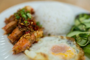 Kızarmış karidesi sarımsak ve biberle karıştırıp buğulanmış pirinçle servis et ve beyaz tabakta yumurta bul.