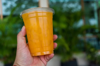 Elinde soğuk taze portakal suyu olan plastik bir bardak.
