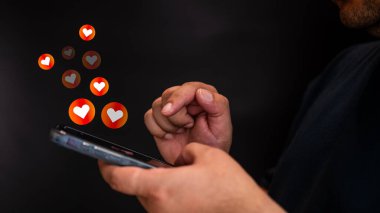 Bir erkek, kalbi simgelerden hoşlanan akıllı telefonu kullanan ellerdir. Sosyal medya, yüzen kalp ikonları sosyal medyanın ilgisini temsil ediyor. Dijital iletişim konsepti. Online randevu