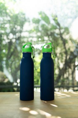 İki mavi asgari yeniden kullanılabilir su şişesi, güneş ışığı olan bir ahşap masada oturuyor.