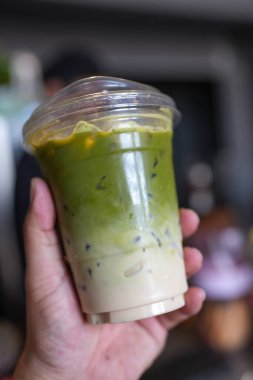 Elinde plastik bardakta buzlu kibrit yeşil latte.