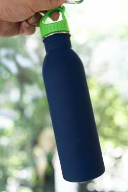 Elinde yeşil kapağı olan şık mavi bir su şişesi. Su içmek için birebirdir..