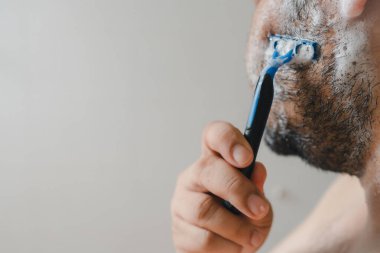 Banyo aynasında sakalını tıraş eden ciddi bir adam.