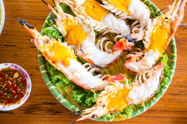 Kömürlü ızgara nehir karidesleri genellikle baharatlı deniz ürünleriyle servis edilir. Karidesin başı yağlı.