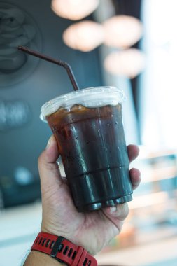 Soğuk americano 'yu plastik bir bardakta kahverengi pipetle tutuyor.