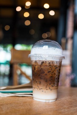 Buzlu Mocha kahvesi, şeffaf plastik bir fincanda servis edilen süt ve kahvenin dokusunu gösteriyor ve kafedeki ahşap masaya koyuyor.