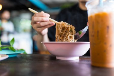 Taylandlı bir adam ahşap çubuklu pembe bir kaseden Tayland erişte çorbası içiyor..