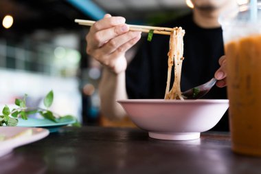 Taylandlı bir adam ahşap çubuklu pembe bir kaseden Tayland erişte çorbası içiyor..