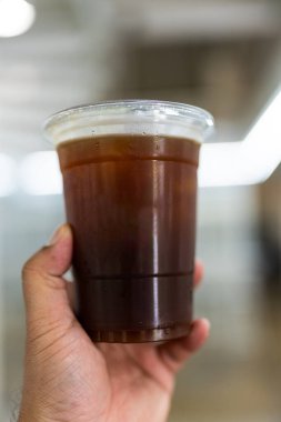 Elinde plastik bir bardak Americano ya da sade kahve tutarken.