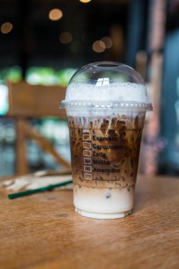 Buzlu Mocha kahvesi, şeffaf plastik bir fincanda servis edilen süt ve kahvenin dokusunu gösteriyor ve kafedeki ahşap masaya koyuyor.