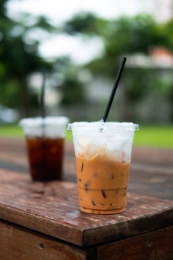 Bahçe kafeteryasındaki ahşap masada içtikten sonra plastik bardakta bir bardak buzlu Thai sütlü çay ve siyah kahve.