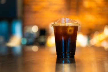 Buzlu, ferahlatıcı bir kahve ya da kahve dükkanındaki turuncu ışık tonunda ahşap masanın üzerindeki Americano restoranını kapatın.