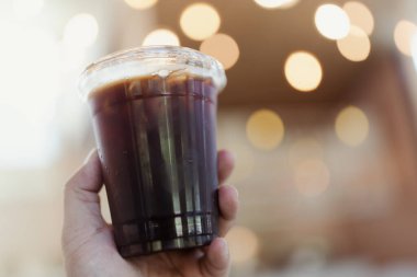 Birisi elinde bokhe arkaplanlı bir fincan buzlu Americano tutsun.