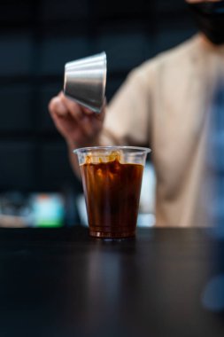 Barista 'nın elleri soğuk su ve buzla bardağa espresso dökerek buzlu sade kahve veya buzlu Americano kahvesi yapar.