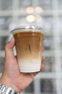 İş adamının elinde iki kat taze süt ve espresso ile bir bardak buzlu latte kahve tutarken yakın plan. Yaz içeceği konseptini tazelemek