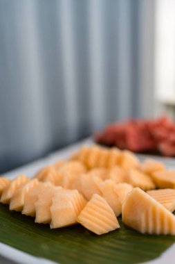 Otel büfesinde muz yaprağı tepsisinde bir dilim kavun. Yemek sırası açık büfe kuyruğunda..