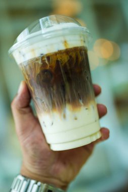Plastik bardakta buzlu karamel macchiato. Elinde taze süt, kahve ve karamel tabakasını vurguluyor.