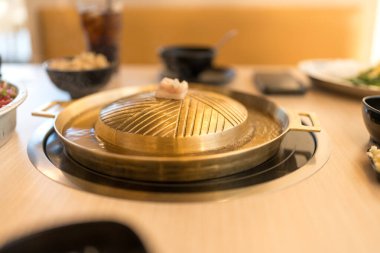 Elektrikli sobanın üzerine boş metalik pirinçli barbekü tavası. Pirinç barbekü tavasında pişmiş domuz eti ve etli Tayland büfesi..