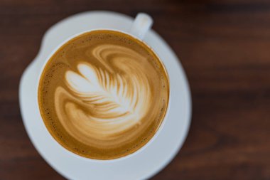 Süt köpüklü latte sanatının sıcak kahve fincanındaki yaprak detaylarını gösteren profesyonel latte sanatını kapat.