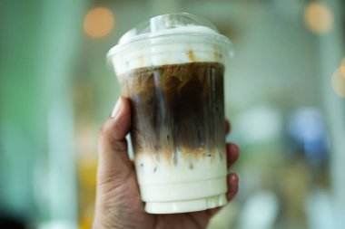 Plastik bardakta buzlu karamel macchiato. Elinde taze süt, kahve ve karamel tabakasını vurguluyor.