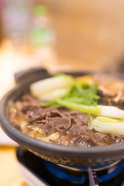 Sukiyaki yemeği ince dilimlenmiş et ve taze sebzeler sunuyor sıcak soya sosu kaynayan bir tencerede pişiyor.