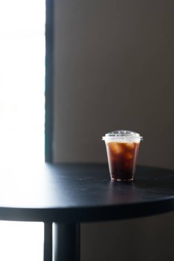 Buzlu Americano siyah ahşap masada tek kullanımlık şeffaf buz kabında.