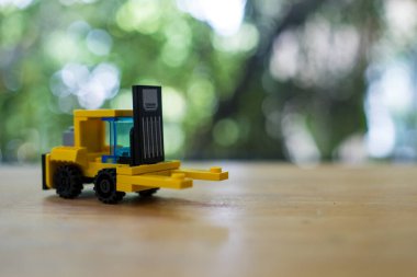Ahşap masada küçük sarı bir forklift modeli. Küçük oyuncak sarı forklift