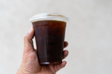 Elinde plastik bir fincan americano kahvesi, yanında şekersiz sade kahve.