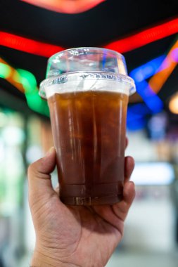 Kafedeki plastik bardakta buzlu sade kahve tutan adam.