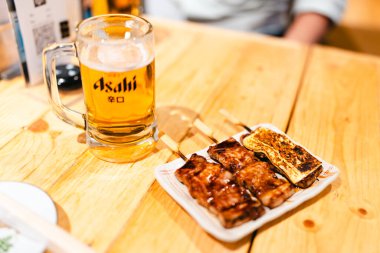 Bangkok, Tayland - 9 Haziran 2025: Bir kupa Asahi, Japon pirinç birası ve izakaya yemekleriyle birlikte Japon arpası.