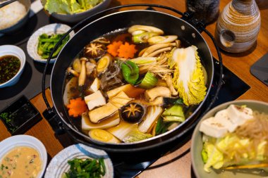 Çorbanın içinde sebze haşlayan adam. İçindekiler de sukiyaki pişiriyor. Canlı sebzelerle kaynayan Sukiyaki güveç tenceresi tadını çıkarmaya hazır.