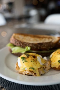 Tabakta yumurtalı Benedict. İçinde haşlanmış yumurta ve holandez sosu var. Seçici odak