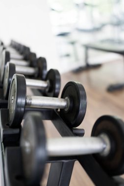 Spor salonunda kuvvet eğitimi için rafüzerinde metal dambıl satır