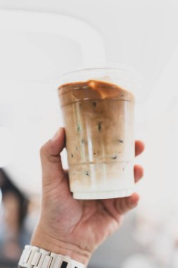 Elinde plastik bardakta buzlu kahve fincanı.