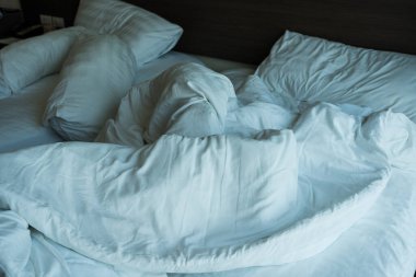 Rahat buruşmuş, buruşuk, dağınık yatak beyaz pamuk çarşaflar, yorgan, battaniye ve yastıklar.