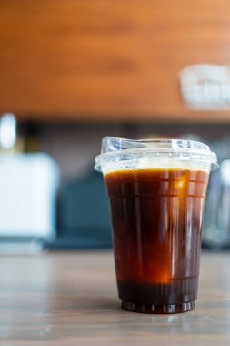 Amerikan kahve bardağını ahşap bir masada buzla tazeliyorum.