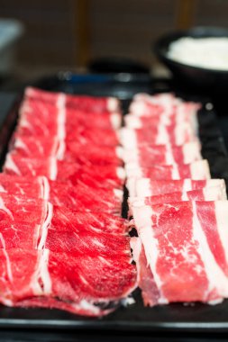 Çiğ et ve çiğ domuz eti kapağı, siyah tepside servis edilir, sıcak tencere tarafından pişirilmeye hazır.