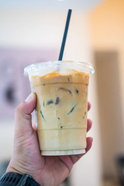 Plastik bardakta pipet ve insan elinin kapağı olsun diye soğuk kahve.